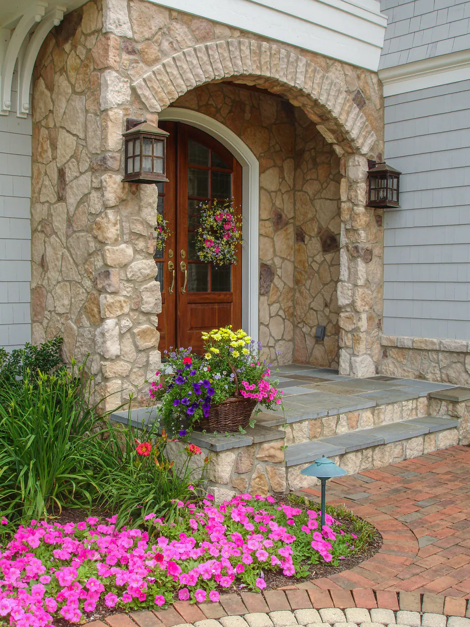 Brick walk leading to stone entry with steps, flower container, magenta planting, and layered garden bed